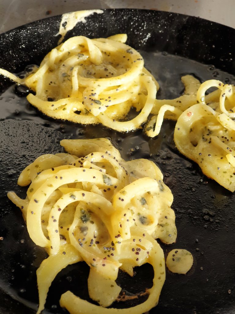 Cast iron frying pan with 3 mock whitebait fritters cooking