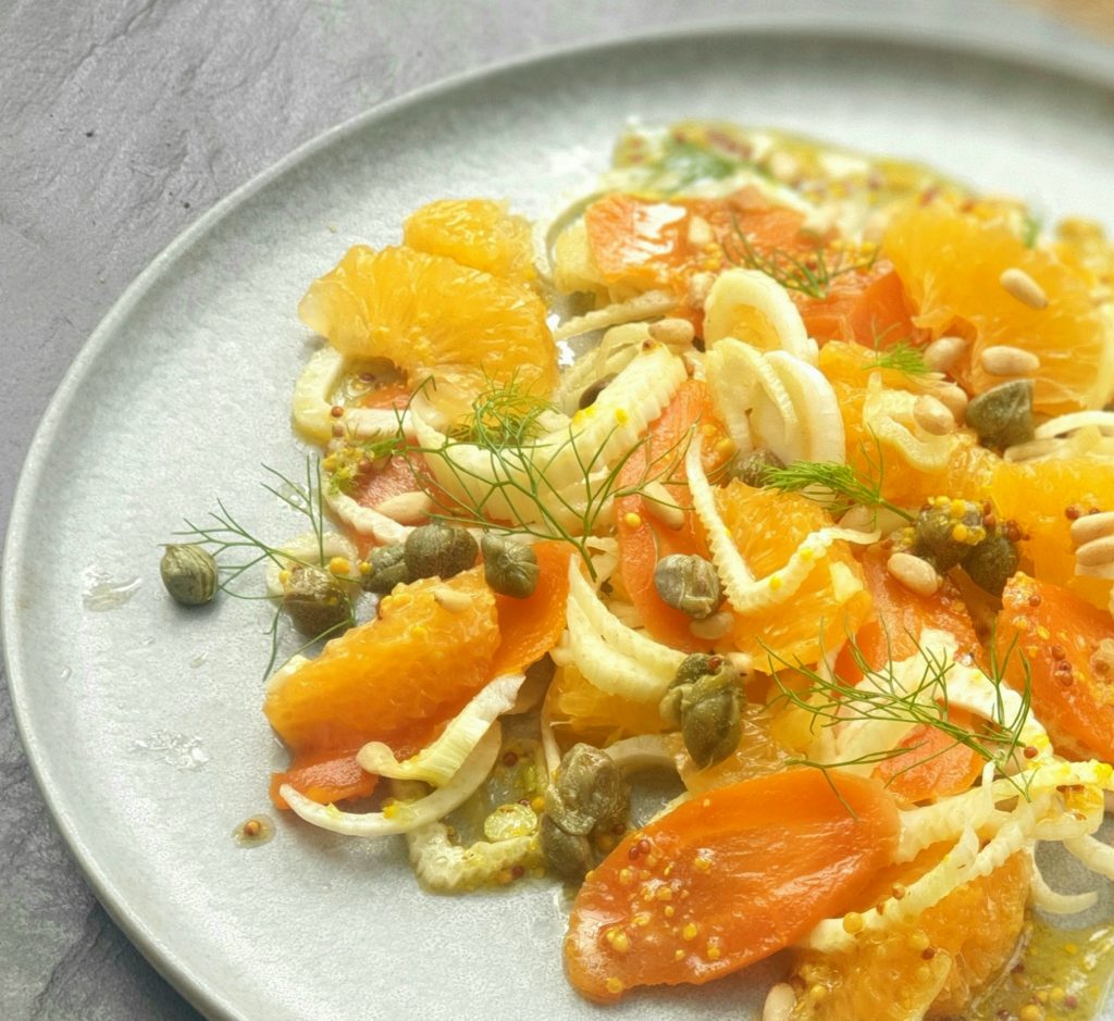 a plate of smoked carrot carpaccio with fennel, grapefruit, capers and pints with a mustard dressing.