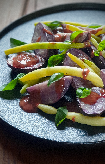 a plate pf purple roasted potatoes with yellow beans drizzled in a raspberry basil vinaigrette
