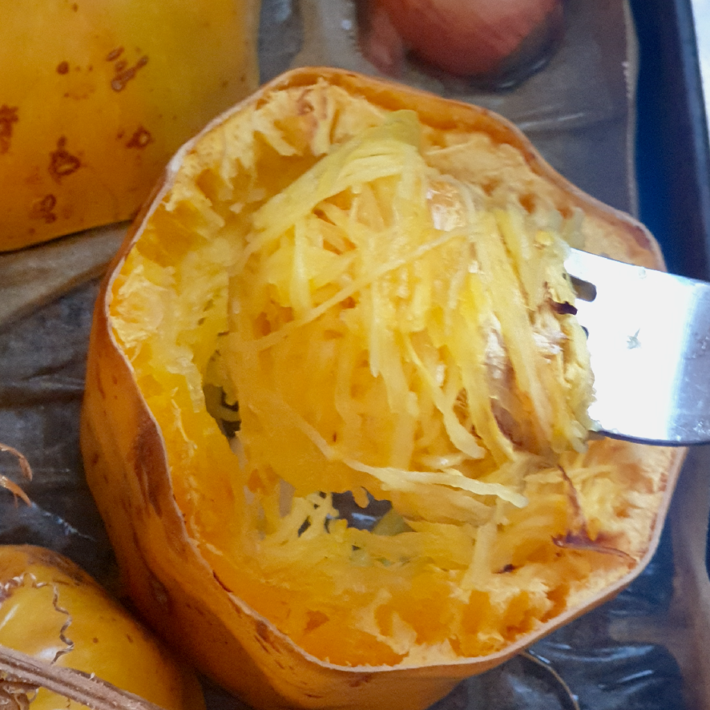 a tray of roasted spaghetti squash being shredded into spaghetti strands