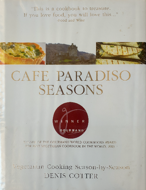 The image is of a cookbook cover titled "Cafe Paradiso Seasons" by Denis Cotter. It features a badge stating "Winner Gourmand," indicating it received the Gourmand World Cookbook Award for Best Vegetarian Cookbook in the World, 2003. The cover includes a quote from Food and Wine saying, "This is a cookbook to treasure. If you love food, you will love this…" There are also two images showing dishes likely from the cookbook, and the subtitle reads "Vegetarian Cooking Season-by-Season," suggesting that the book offers recipes according to the seasons.