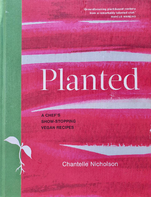 The cookbook cover shows the title "Planted" in large white letters against a pink background with brushstroke textures. Below the title, it reads "A Chef's Show-Stopping Vegan Recipes." The author's name, "Chantelle Nicholson," is prominently displayed at the bottom. A small white icon of a sprouting plant is near the bottom left. The spine of the book is in a contrasting green color. There's a praise quote at the top: "Groundbreaking plant-based cookery from a remarkably talented chef," attributed to Marcus Wareing.