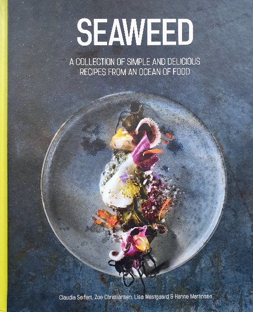 Cover of the cookbook titled 'Seaweed,' featuring a sophisticated dish with vibrant edible flowers and dark seaweed on a textured gray plate. The cover highlights the book as 'A Collection of Simple and Delicious Recipes from an Ocean of Food.