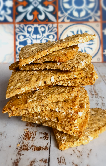 A stack of quarter-circle shaped potato and seaweed Scottish oatcakes artfully arranged, with a rustic blue and white tiled background enhancing the golden-brown hue of the oatcakes.