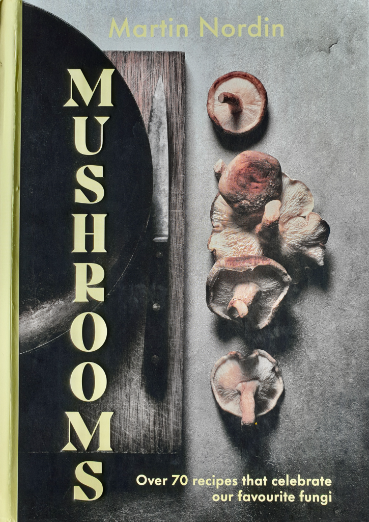 The book cover image is titled "Mushrooms" by Martin Nordin. The tagline reads, "Over 70 recipes that celebrate our favourite fungi." The cover features an arrangement of various mushrooms and a knife placed on a wooden surface