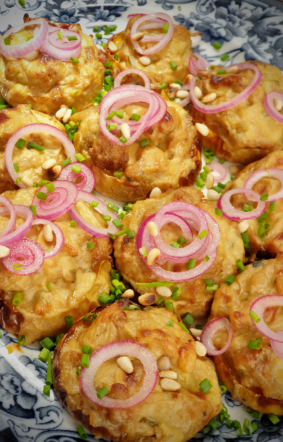 rounds of golden dairy - free cauliflower cheese on roasted slices of butternut garnished with pickled onions on a blue and white patterned platter