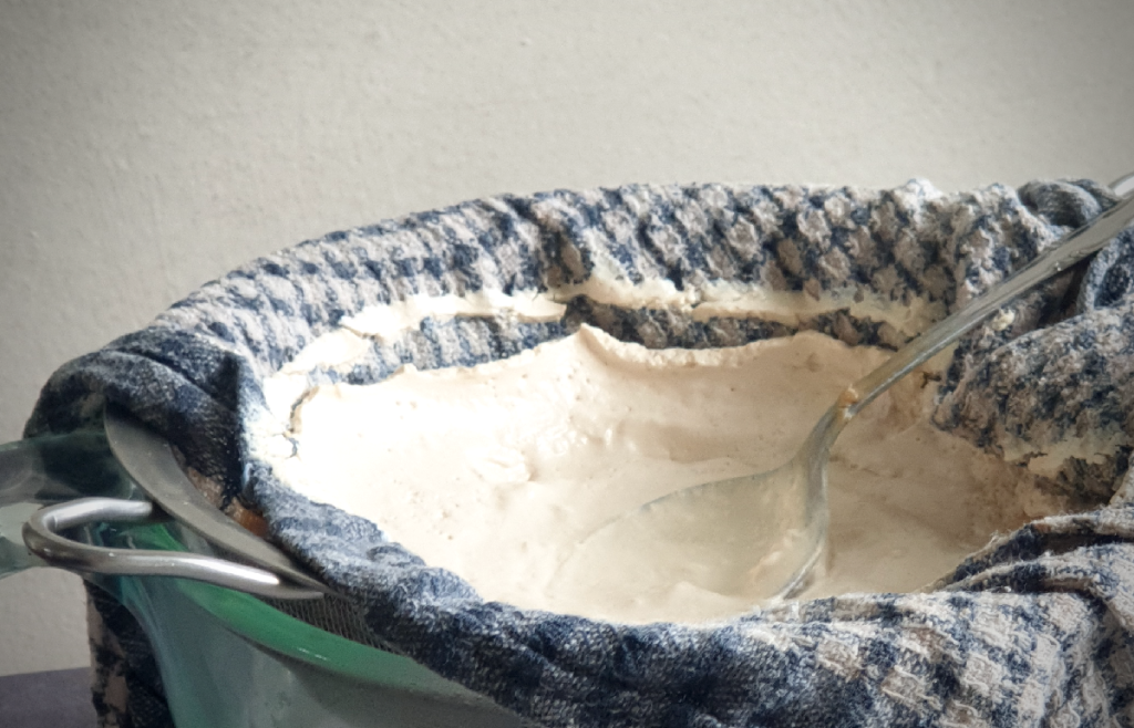 a pyrex jug with a blue checked cotton towel in a sieve straining soy sour cream